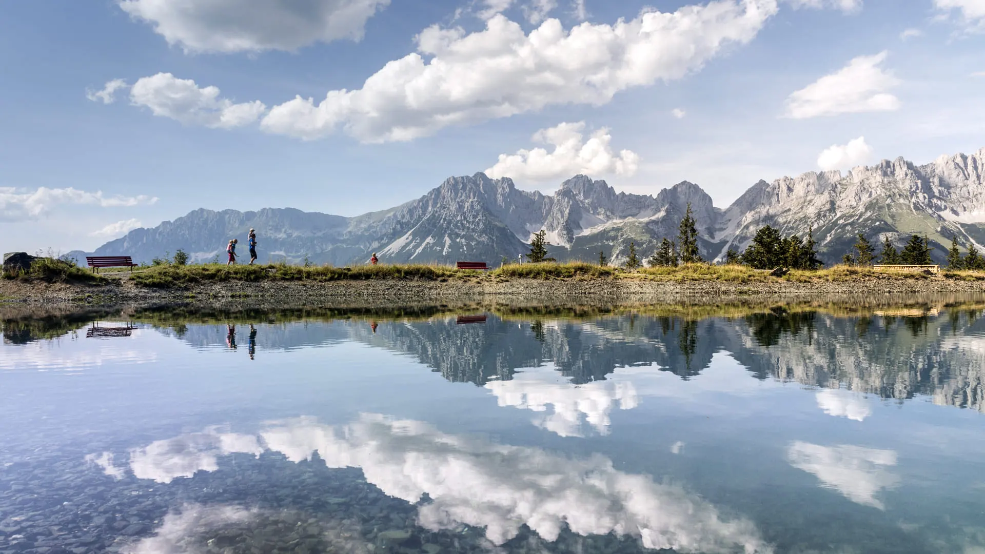 Blick auf Astbergsee mit reflektierenden Bergen und zwei Personen am Ufer