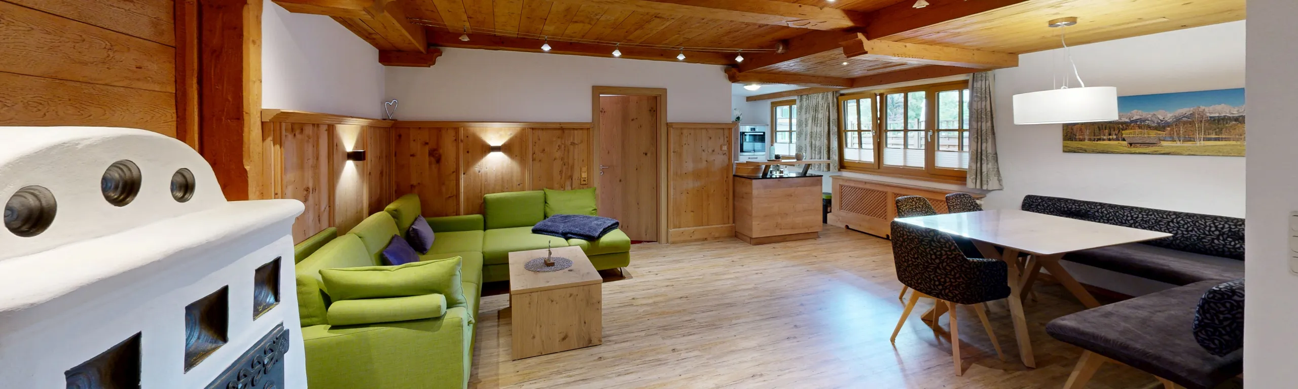 Helle Wohnküche mit grünen Sofas, Holzverkleidung und Essbereich.