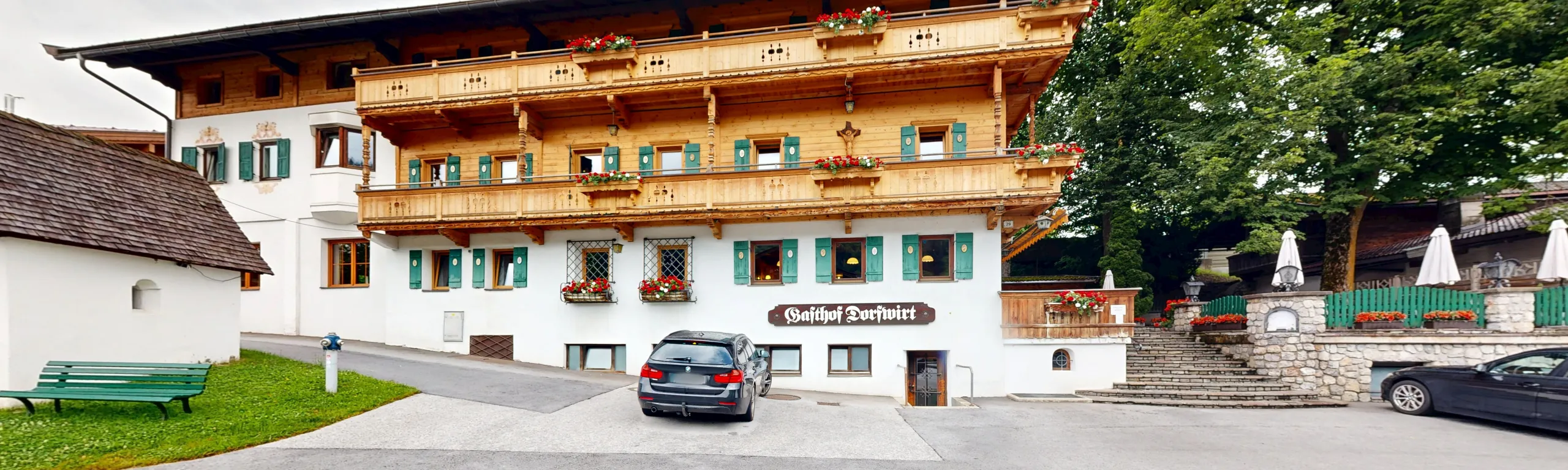 Mehrstöckiges Gebäude mit Holzbalustraden und Blumen, Parkplatz vorne.