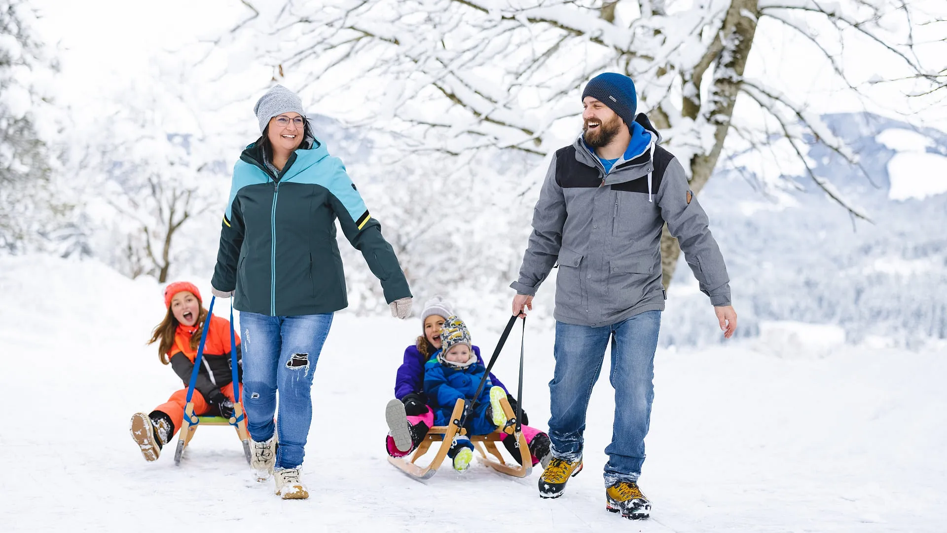 Familie zieht Schlitten mit Kindern durch verschneite Winterlandschaft