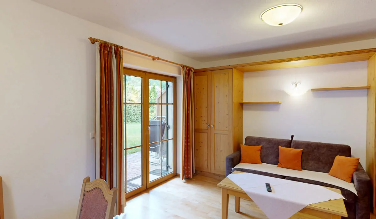 Wohnraum mit Fenster, Couch, Tisch und Zugang zur Terrasse