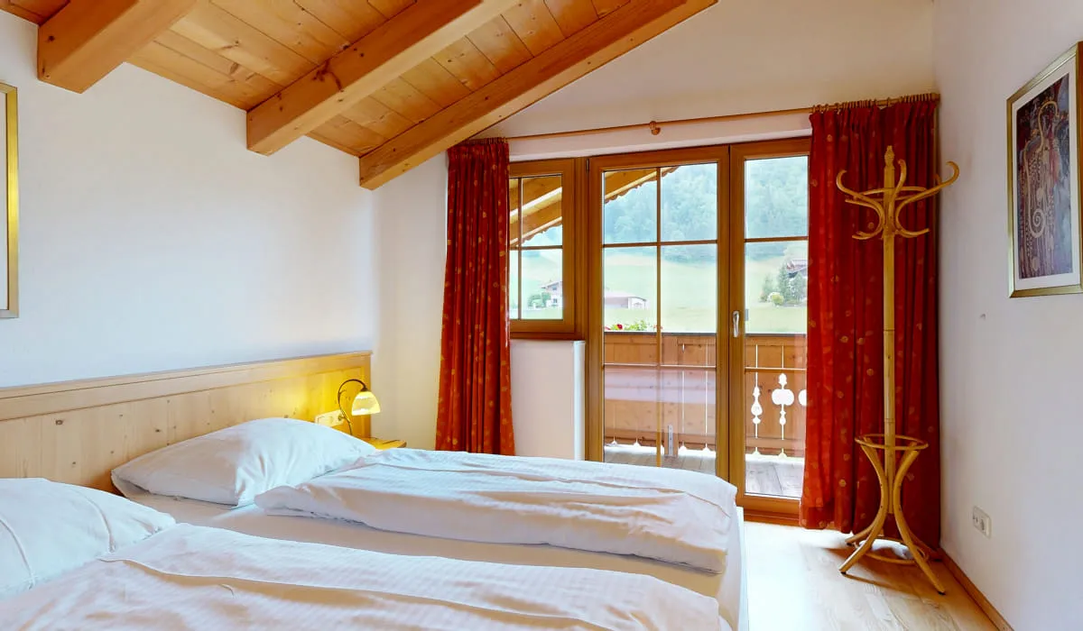 Gemütliches Schlafzimmer mit zwei Betten, Balkon und roten Vorhängen.