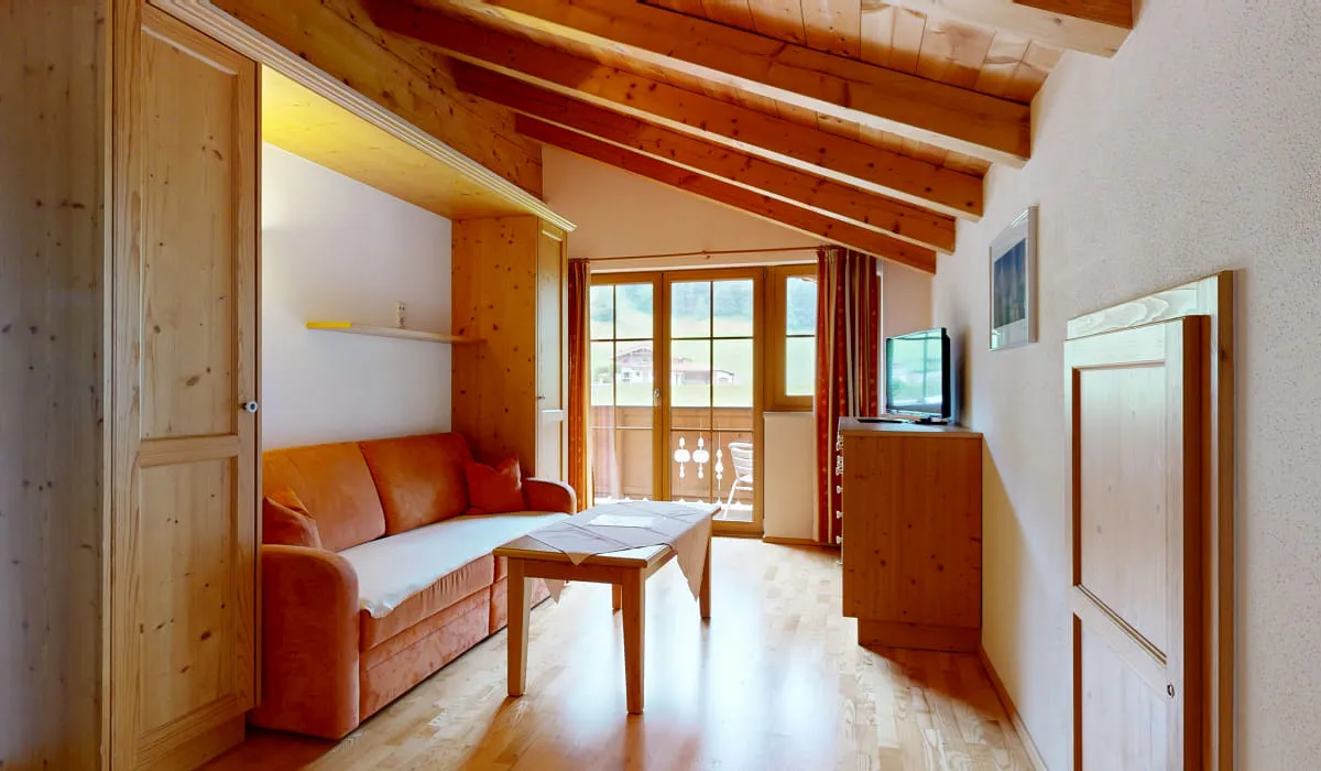 Heller Wohnraum mit Holzwänden, orangefarbenem Sofa und Fenster mit Aussicht.