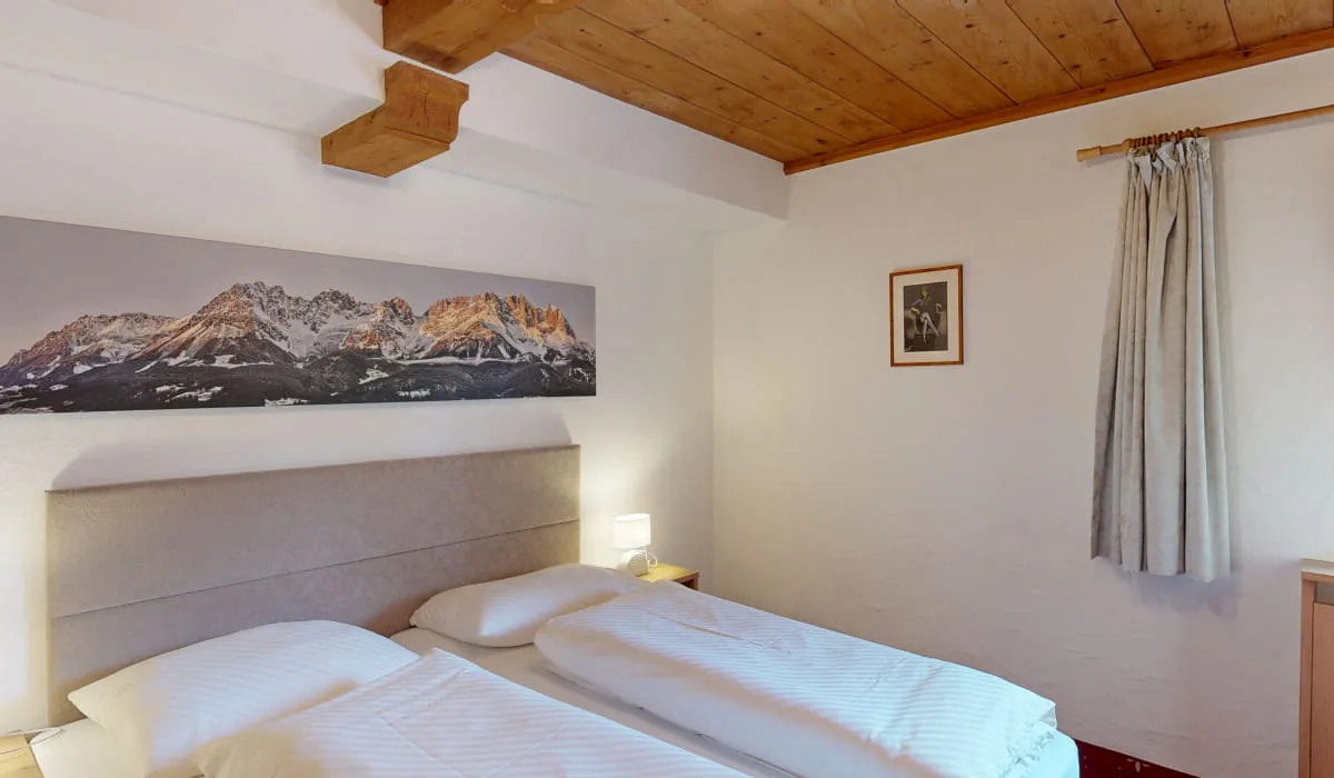 Schlafzimmer mit zwei Betten, Holzbalkendecke und Bergbild an der Wand.
