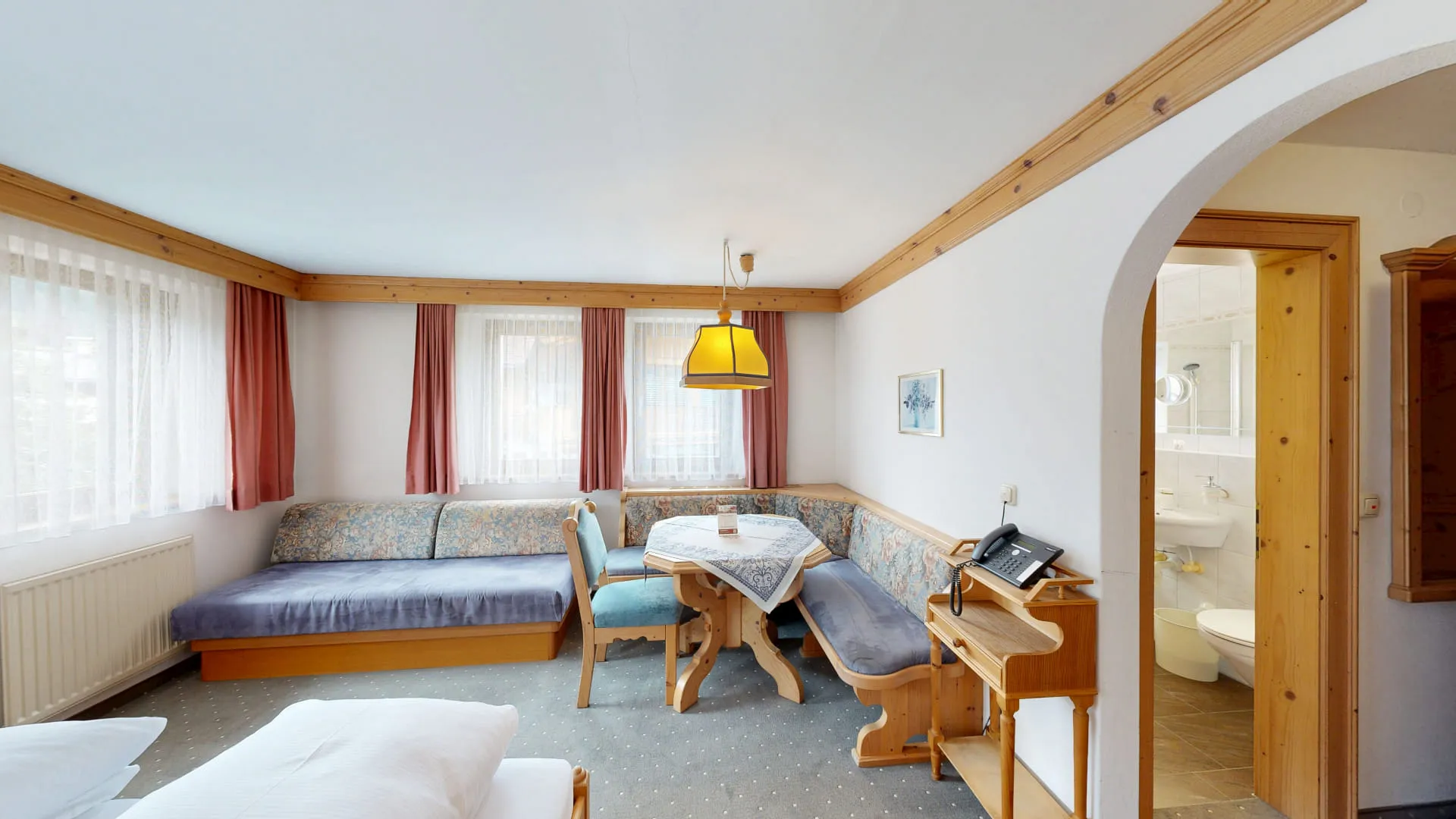 Helle Zimmeransicht mit Sofa, Tisch, Stuhl und Zugang zum Badezimmer.