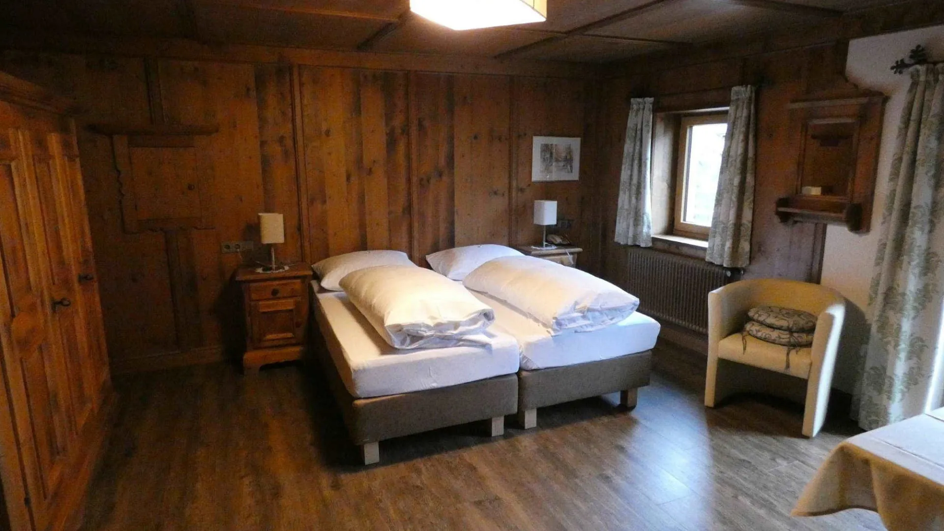 Gemütliches Zimmer mit Holzverkleidungen, zwei Betten und Sessel.